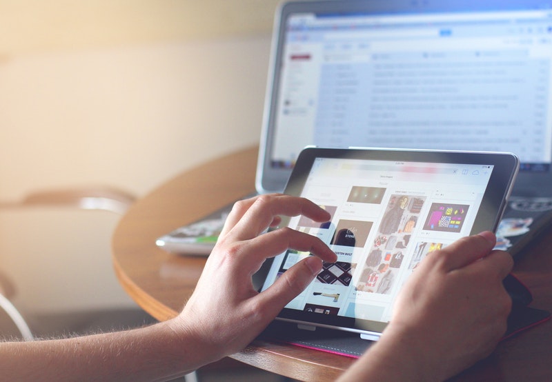 person holding tablet, next to computer